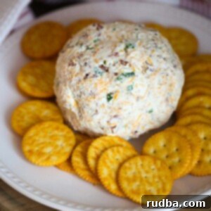 Timeless Cheese Ball Perfection 2 Classic cheese ball coated in nuts and bacon, beautifully presented on a white serving plate surrounded by an assortment of crisp crackers.