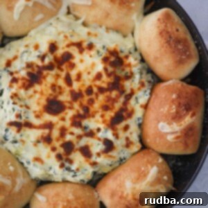 Ultimate spinach artichoke dip with dinner rolls on the side.