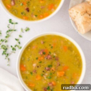 Two small bowls filled with split pea soup with ham and herbs and bread on the side.