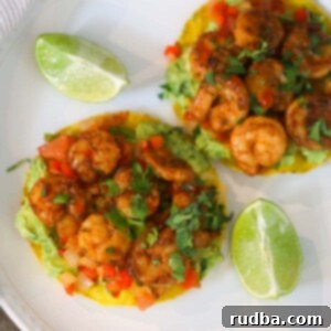 Two shrimp tostadas on a white plate with lime wedges on the side.