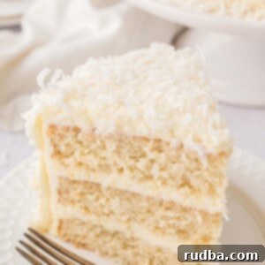 Southern Coconut Cloud 2 A slice of coconut cake on a white plate with a fork.