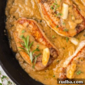 Juicy Pan-Seared Pork Chops with Velvety Gravy 2 pan seared pork chops with gravy in a cast iron skillet.