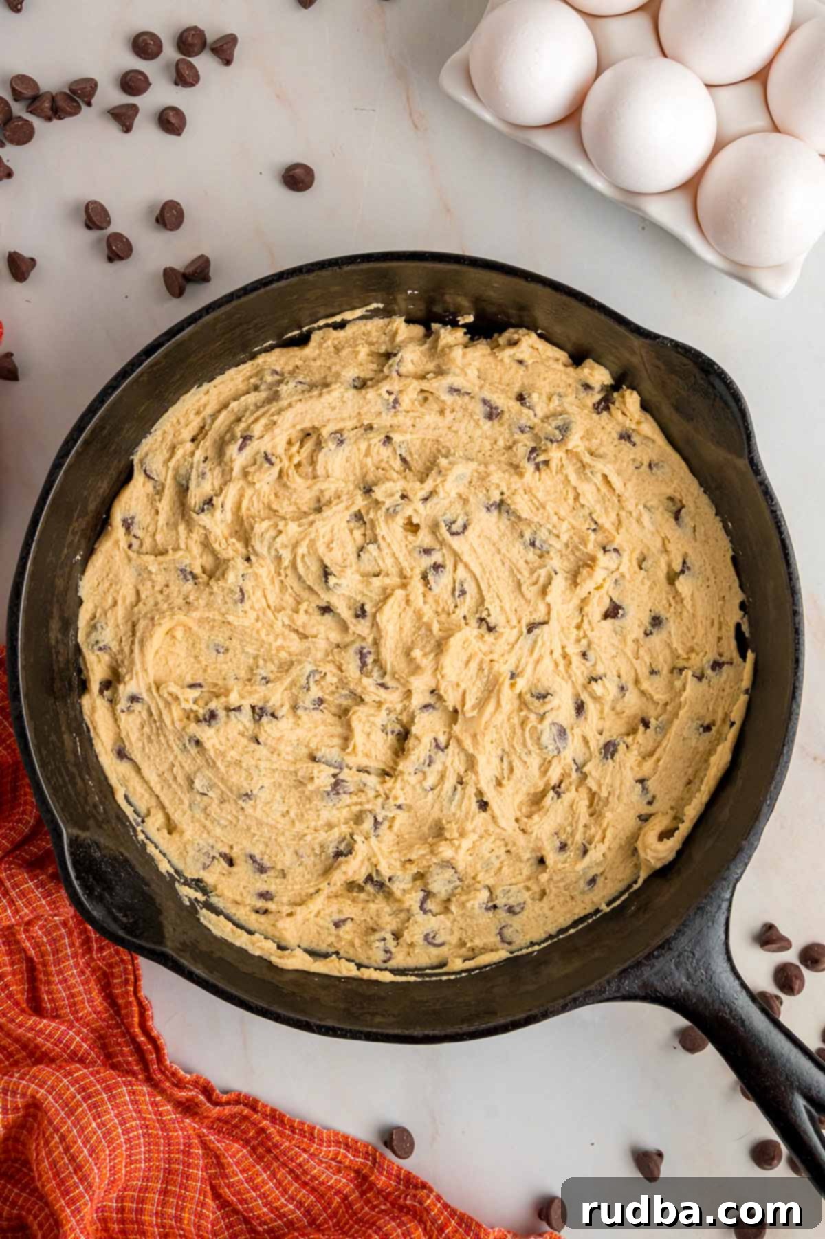 Cookie dough in a 10-inch iron skillet with eggs and chocolate chips on the side.