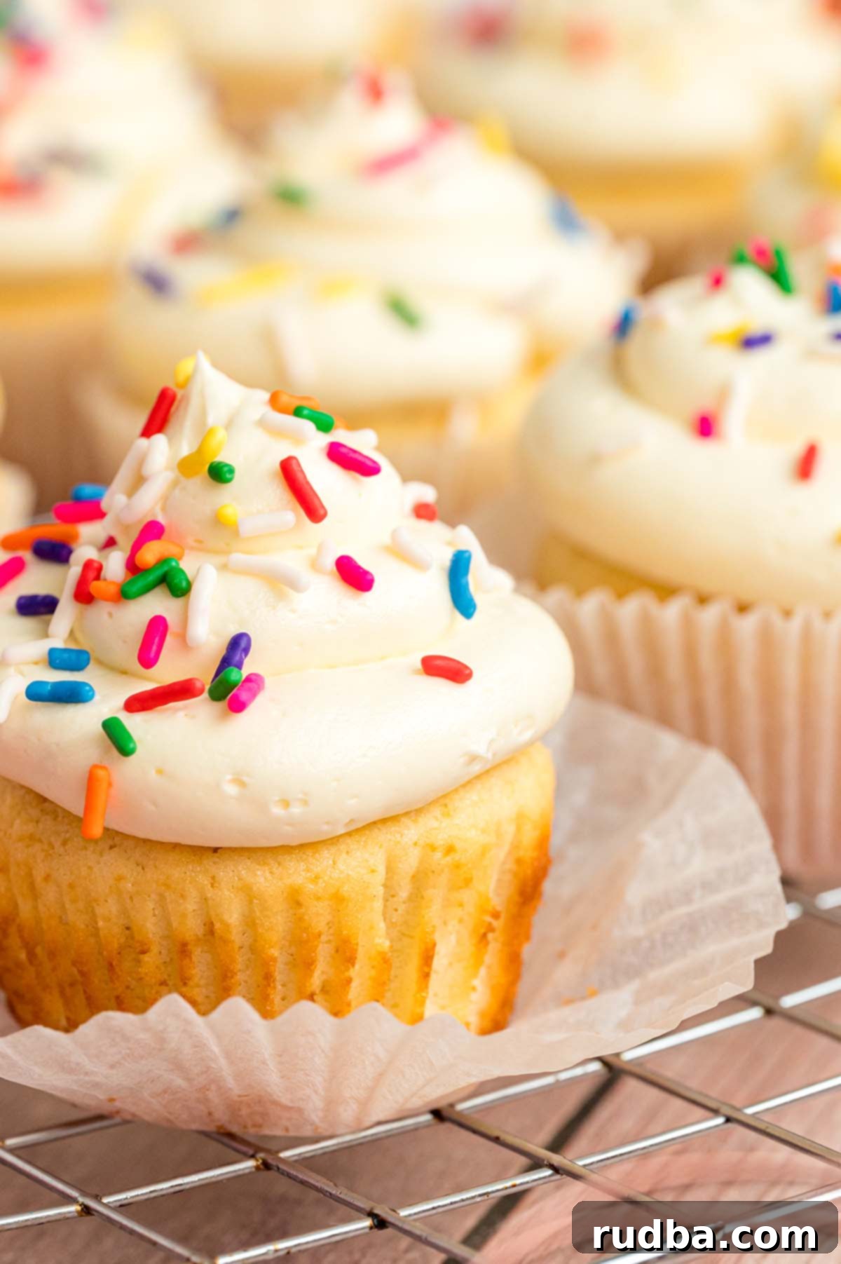 Velvety Vanilla Cupcakes 2 A beautifully decorated vanilla cupcake with smooth white frosting and vibrant rainbow sprinkles, ready for enjoyment.