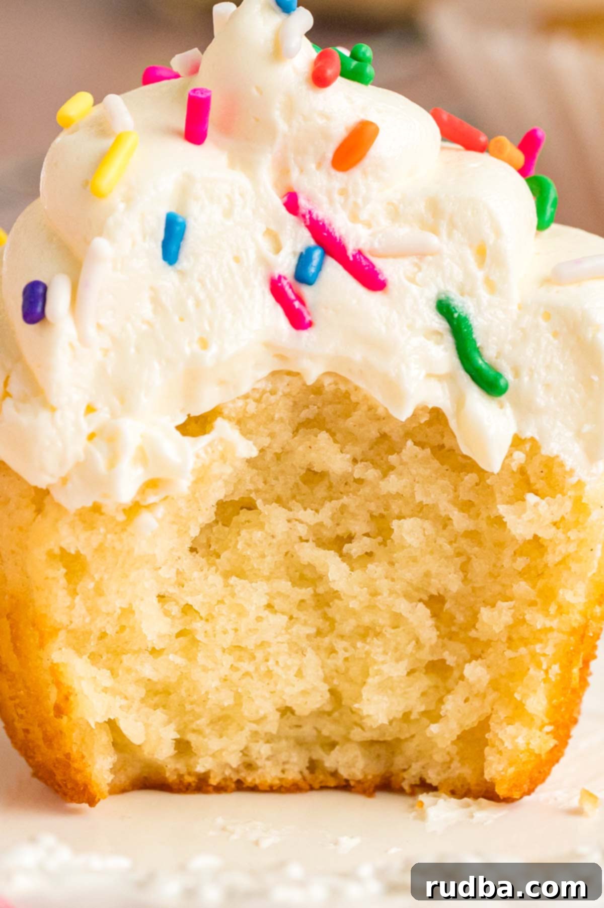 Velvety Vanilla Cupcakes 5 An enticing close-up of a bitten vanilla cupcake, revealing its fluffy interior and smooth frosting.
