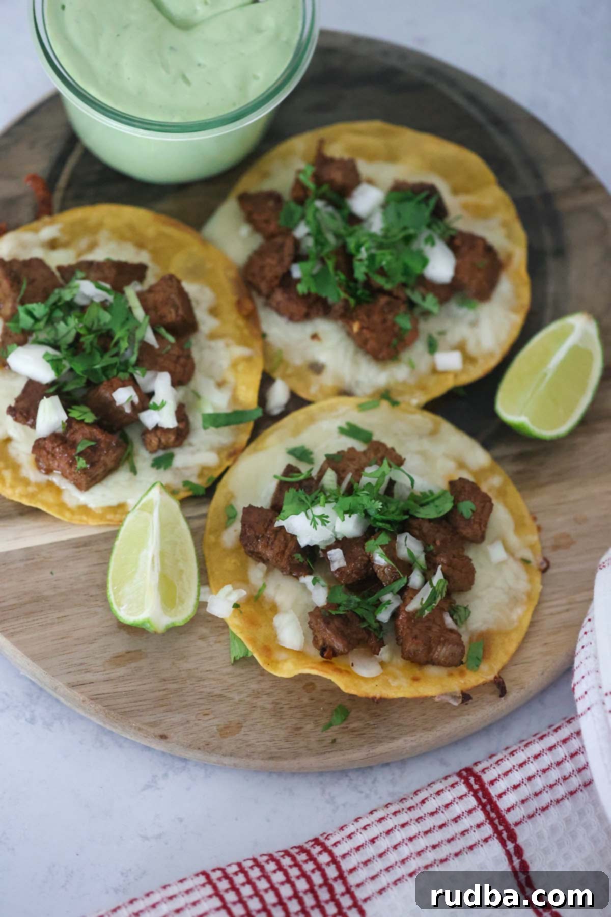 Sizzling Steak Tacos 2 Three steak tacos with lime wedges and avocado crema on the side, ready to be served.