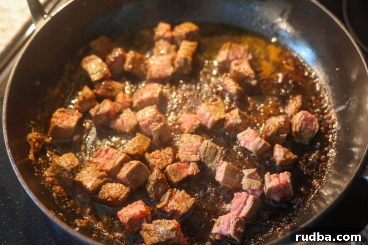 Sizzling Steak Tacos 4 Steak pieces cooking in a hot cast iron skillet on the stovetop, sizzling and browning.