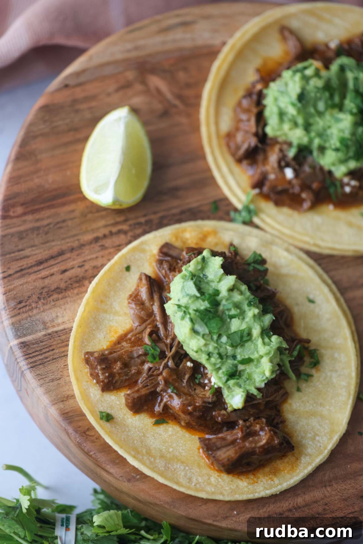 Two shredded beef tacos on a wooden board with a lime wedge on the side, ready to be enjoyed.