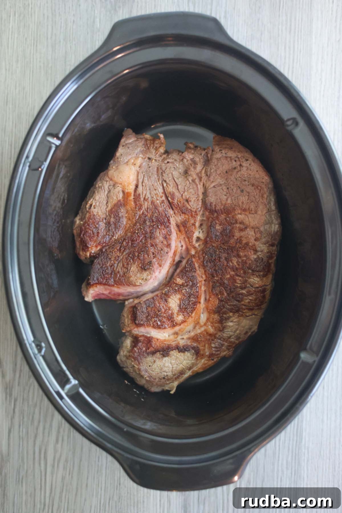 Seared chuck roast beef in a slow cooker, showing its delicious browned crust.