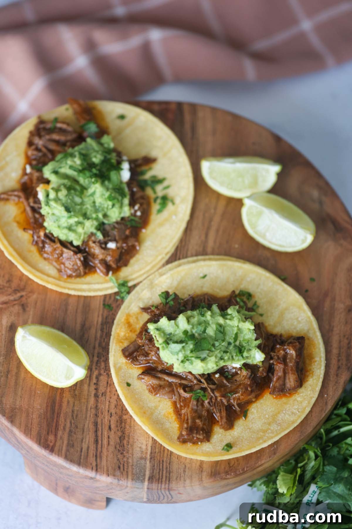 A close-up view of two generously filled shredded beef tacos, highlighting the tender meat and toppings.