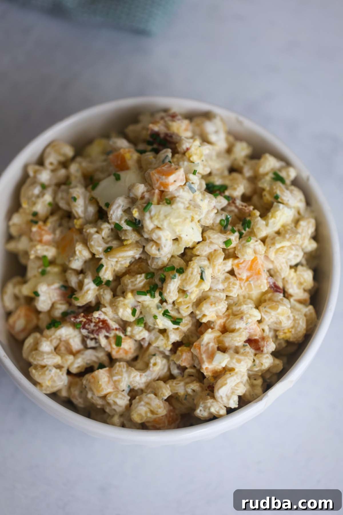Creamy bacon ranch pasta salad served in a pristine white bowl, garnished with fresh chives and extra bacon bits, highlighting its rich texture and appetizing appeal.