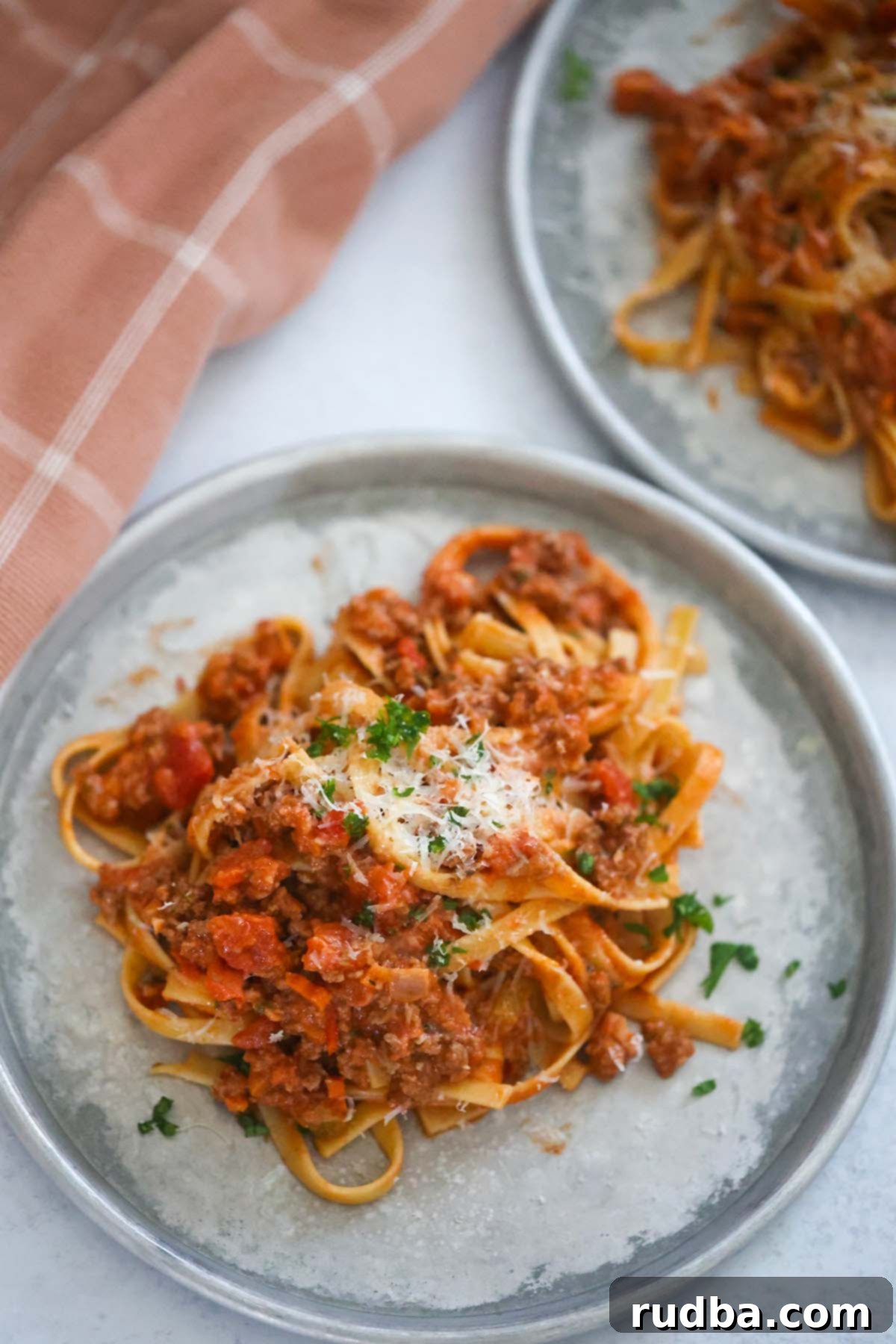 Indulgent Fettuccine Bolognese 2 Two plates of fettuccine bolognese with a towel on the side.