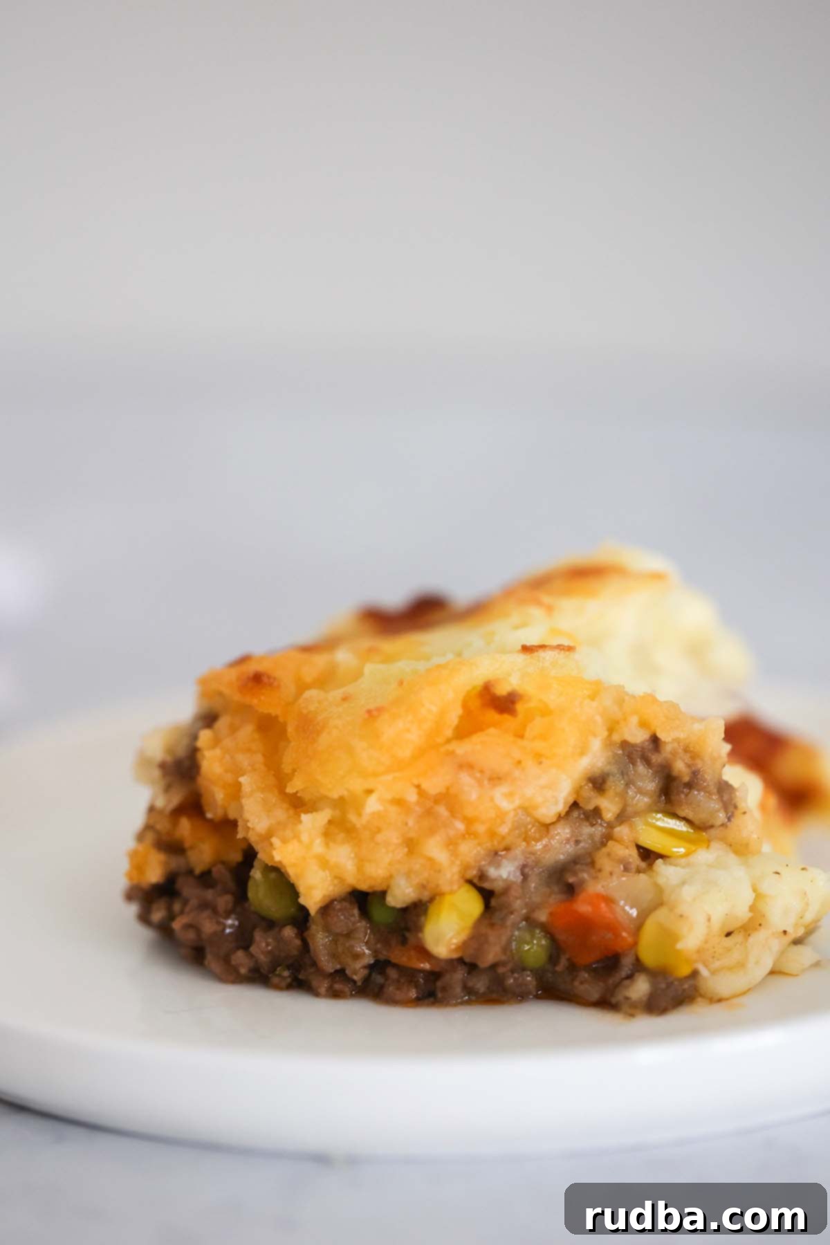Golden Crust Beef and Mash 5 A perfectly portioned slice of golden-crusted Cottage Pie resting on a white plate, revealing its savory layers.
