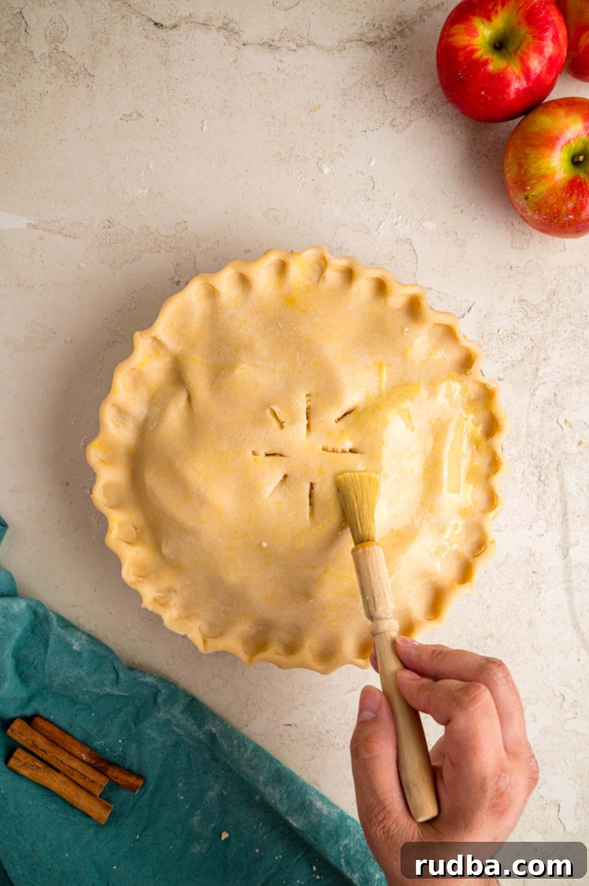 Warm Spiced Apple Pie 6 A pastry brush applying an egg wash to the top of an assembled apple pie, ready for baking.
