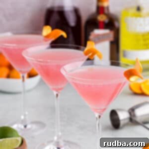 Classic Cosmopolitan Cocktail Recipe 6 Three cosmopolitan martinis with alcohol bottles in the background.