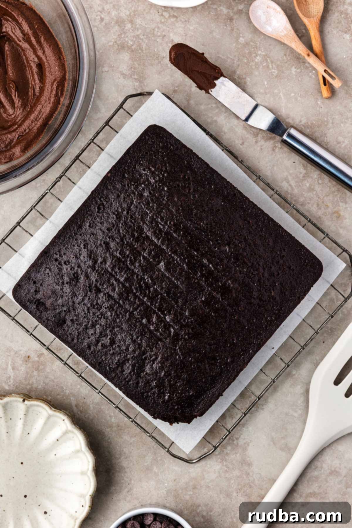 Chocolate Wacky Cake 4 An 8x8 inch baked chocolate wacky cake, perfectly cooled, with a bowl of creamy homemade chocolate frosting ready on the side for spreading.