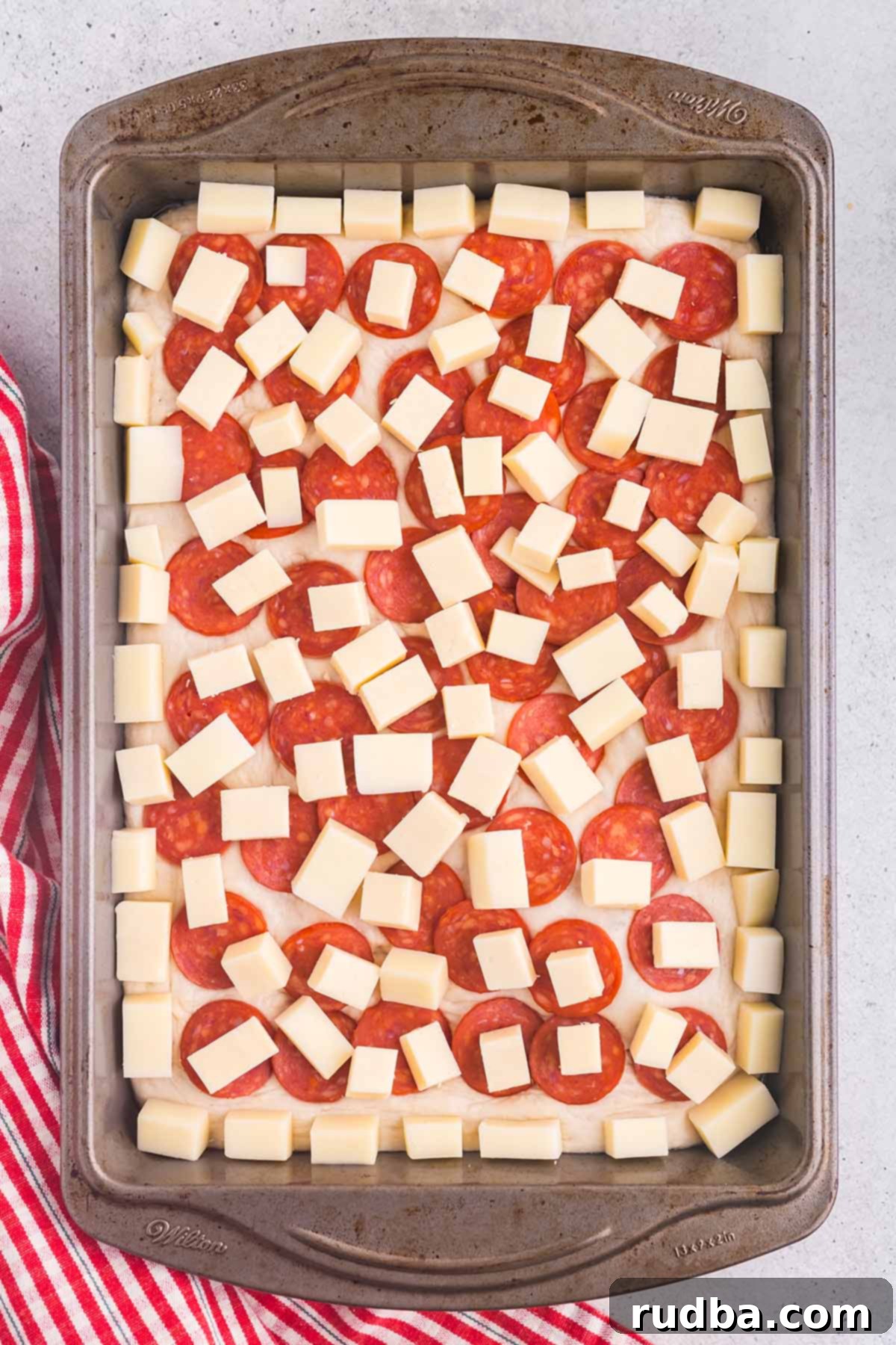 Classic Detroit Style Pan Pizza 5 Close-up of an unbaked Detroit style pan pizza, beautifully layered with melted cheese, vibrant red sauce stripes, and perfectly arranged cup-and-char pepperoni, ready for the oven.