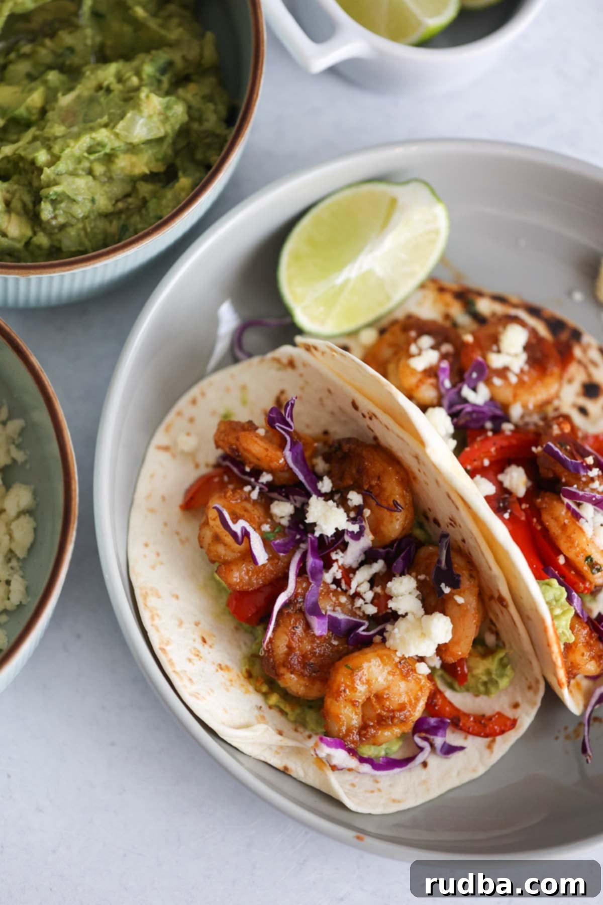 Zesty Shrimp Tacos 2 Two shrimp tacos with guacamole, limes, and cotija cheese on the side.