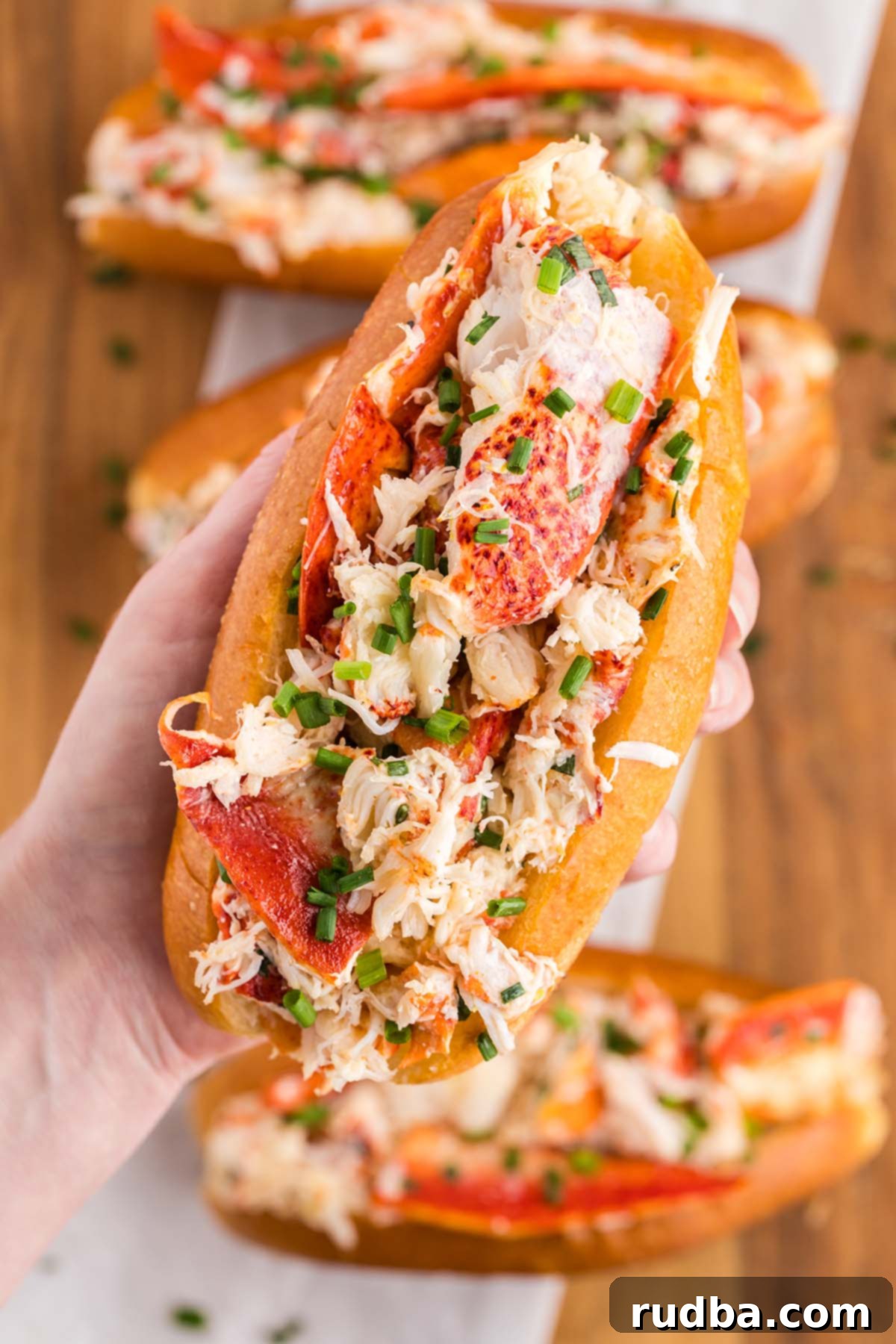 A close-up shot of a hand holding a perfectly assembled lobster roll, showcasing the generous filling and toasted bun.
