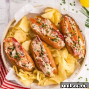 Four classic lobster rolls with a side of potato chips, pickles, and lemon wedges.