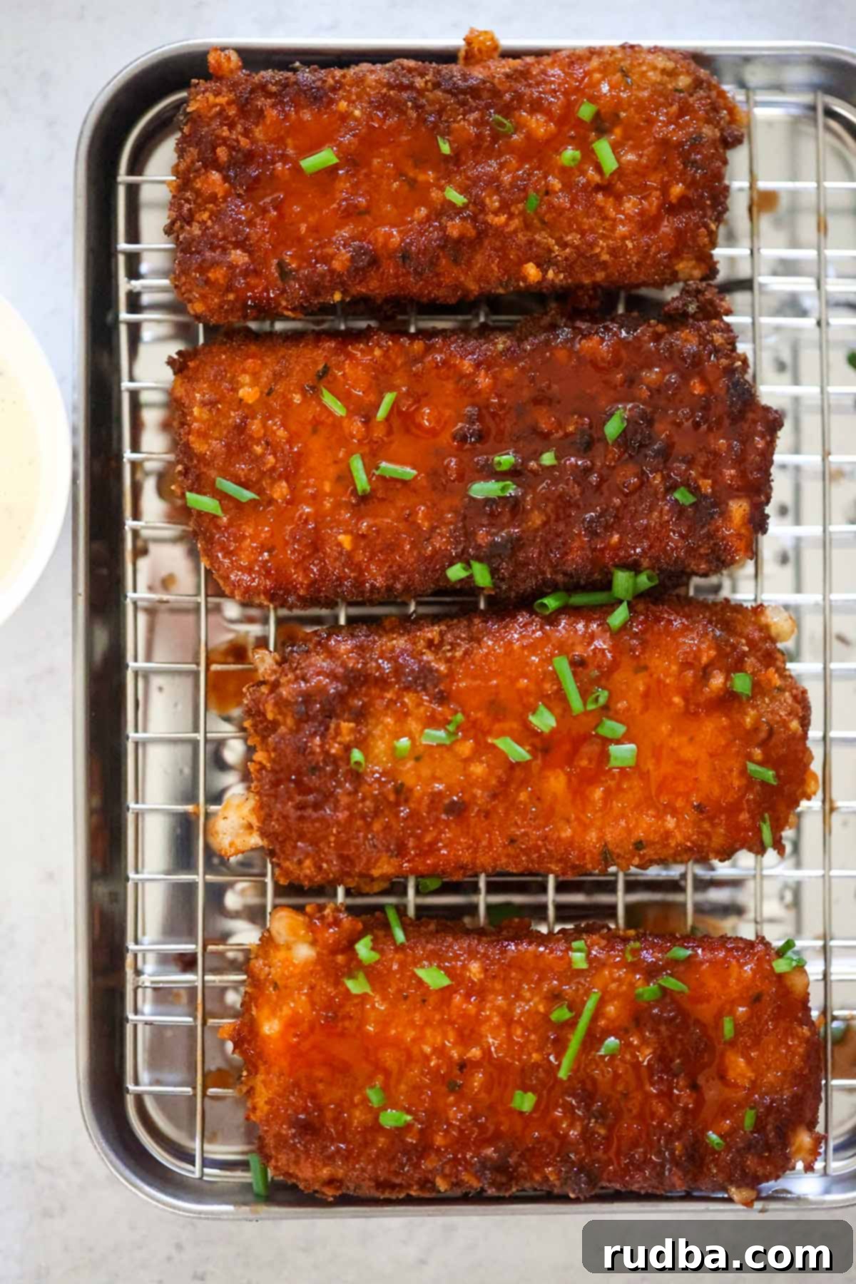 Honey Chipotle Mozzarella Poppers 2 Four honey chipotle fried mozzarella sticks on a rack, freshly fried and gleaming with sauce.