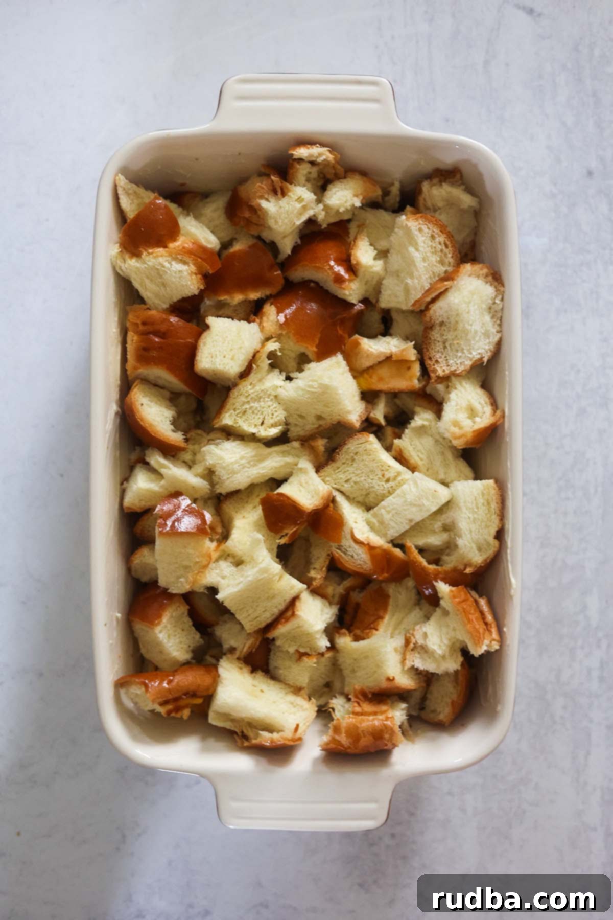 Authentic Cuban Bread Pudding 4 Cubes of stale challah bread perfectly arranged in a greased baking dish, ready to be drenched in creamy custard before baking. The texture of the bread shows it's ideal for absorption.