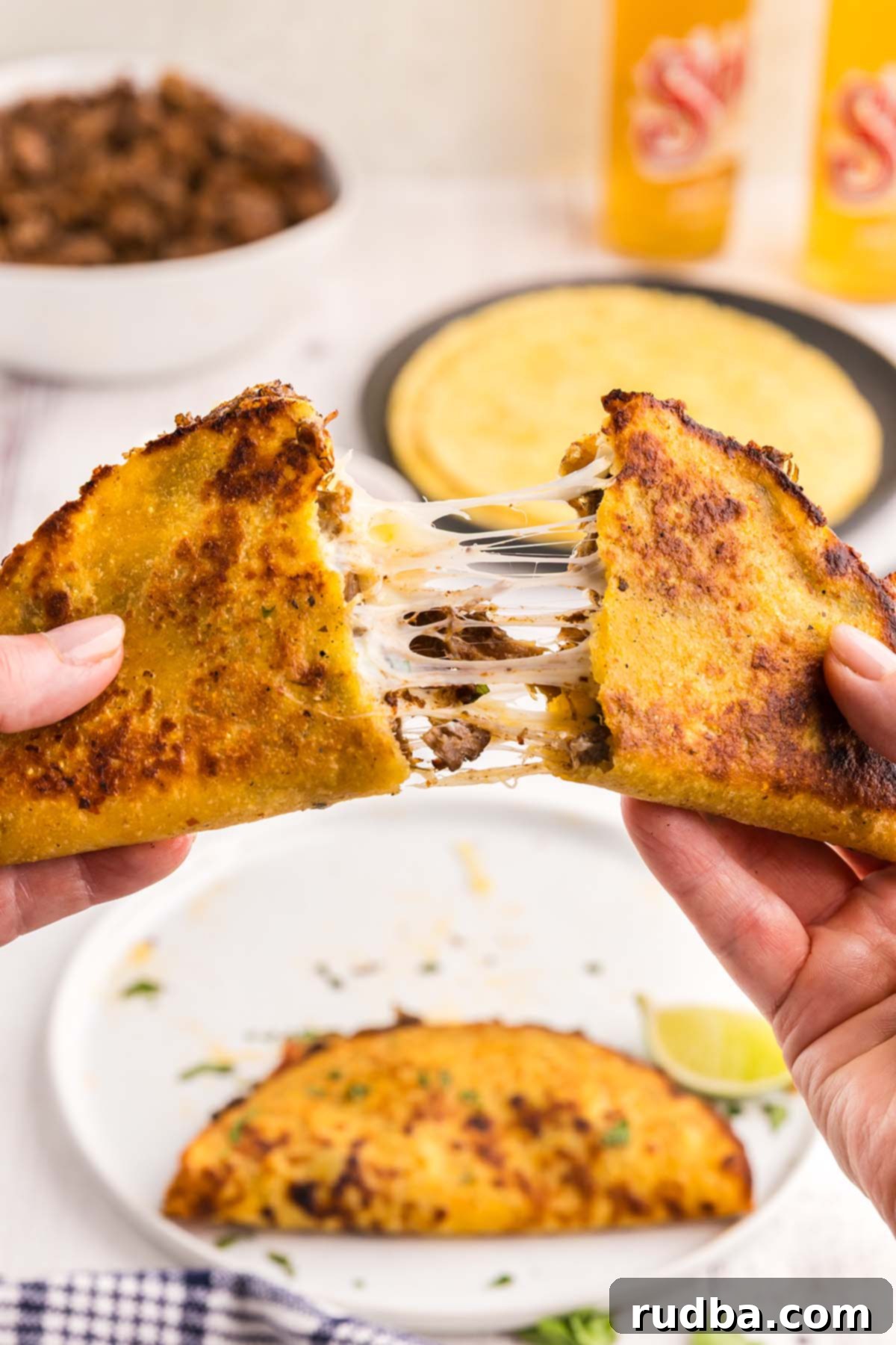 A hand holding up a crispy birria taco filled with juicy beef and melted cheese, ready for dipping.