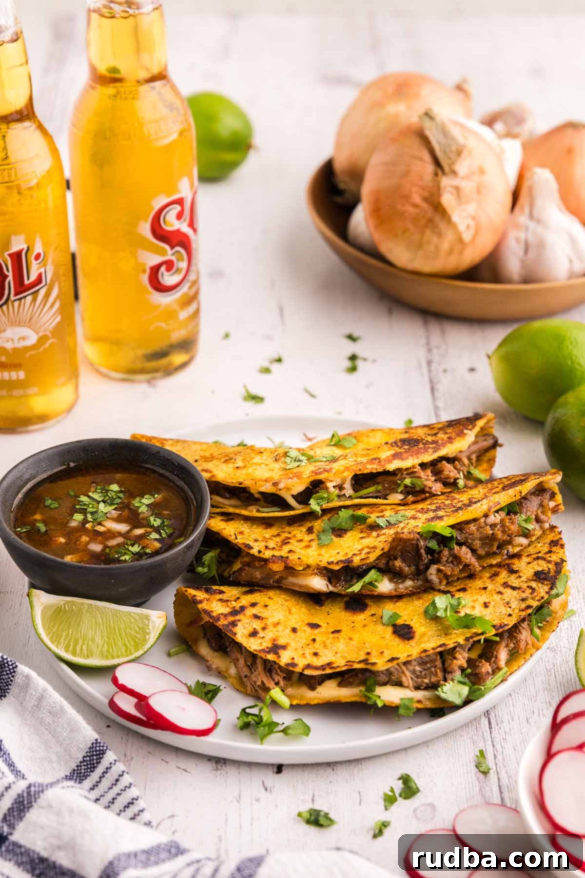 Three perfectly cooked birria tacos, golden and crispy, served alongside small bowls of rich consomé, fresh lime wedges, and refreshing sodas, highlighting a complete meal setup.