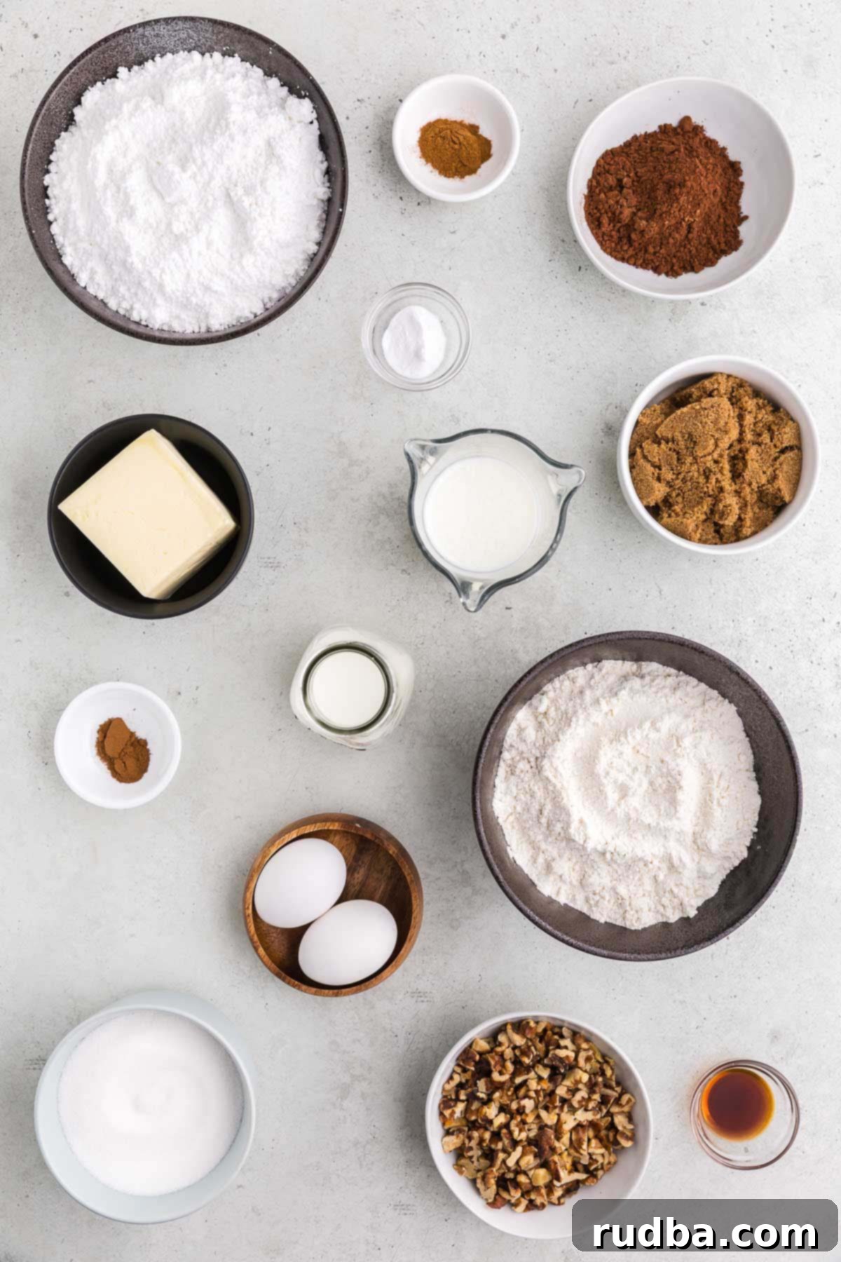 Assortment of fresh ingredients for Texas Sheet Cake: eggs, milk, vanilla extract, butter, cocoa powder, flour, and sugars, neatly arranged on a kitchen counter.