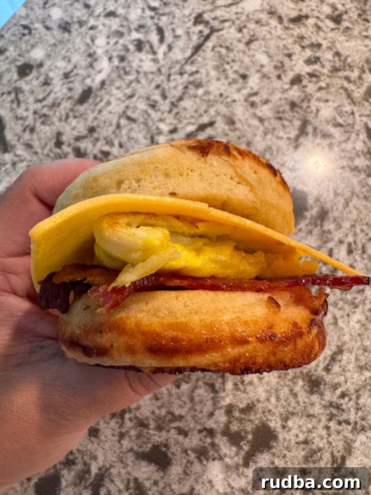 A hand holding a McGriddle sandwich with bacon, egg, and cheese between two pancakes.