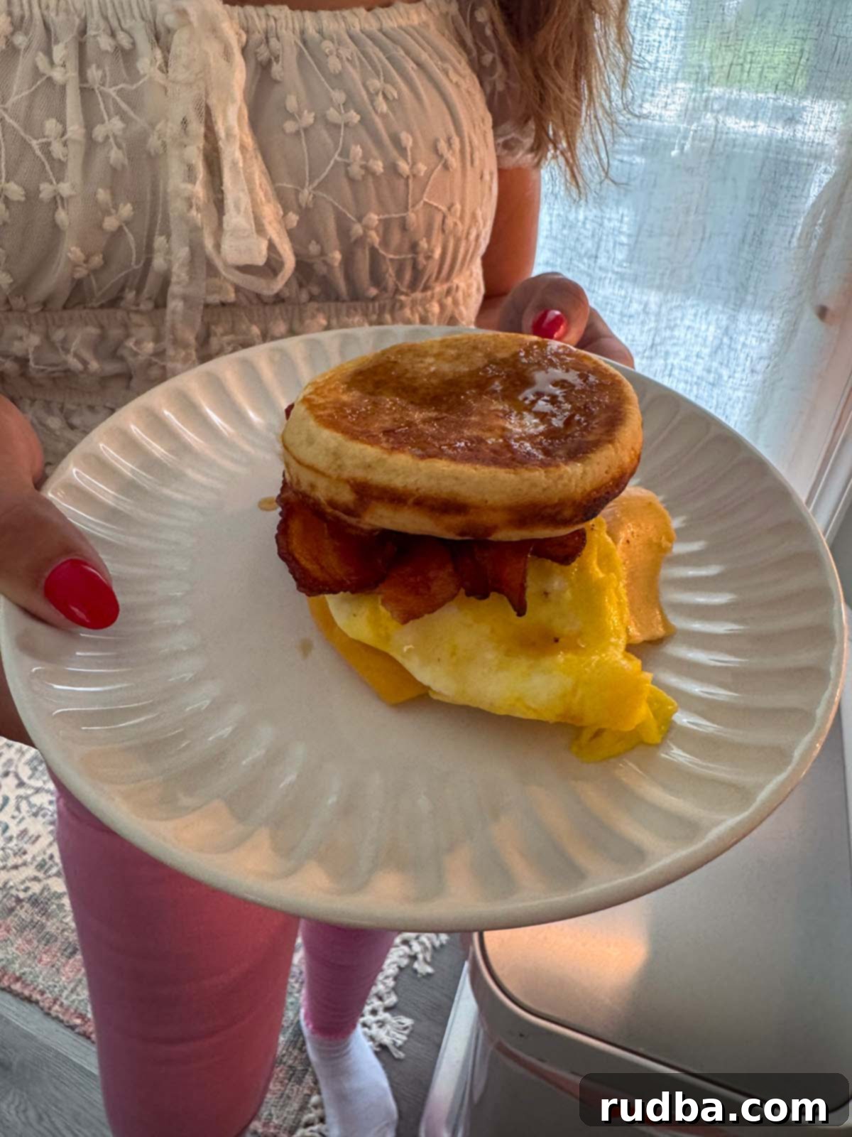 A person holding a McGriddle sandwich on a white plate, showcasing the layers.