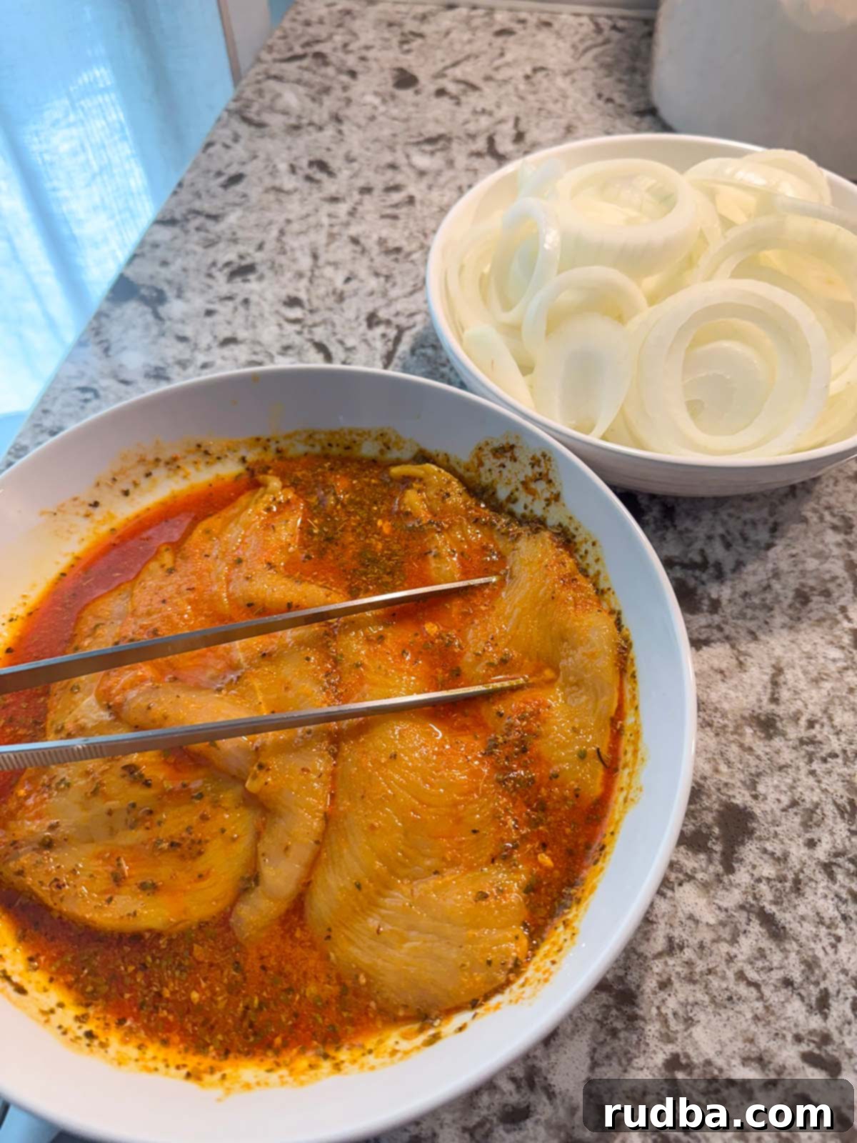 Zesty Cuban Pan-Seared Chicken 3 Raw chicken breasts soaking in a vibrant citrus and spice marinade, with thinly sliced raw onions on the side, ready for cooking.