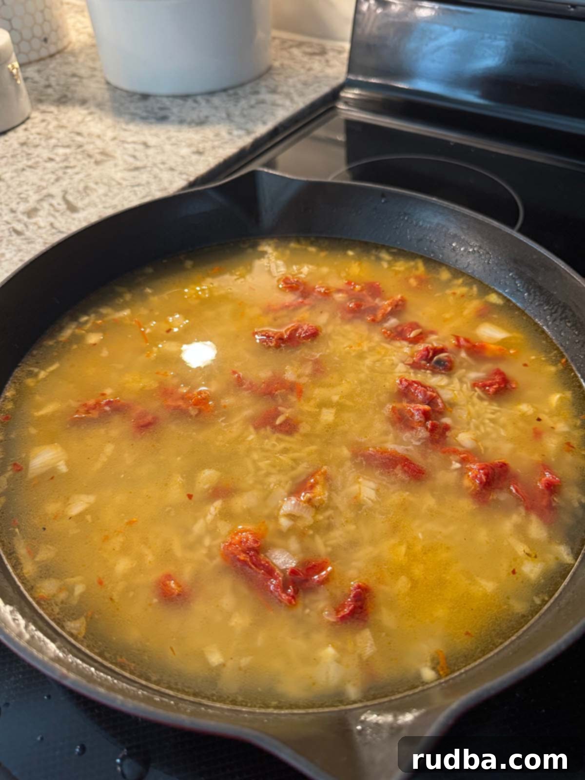 Orzo simmering in a cast iron skillet on the stove.