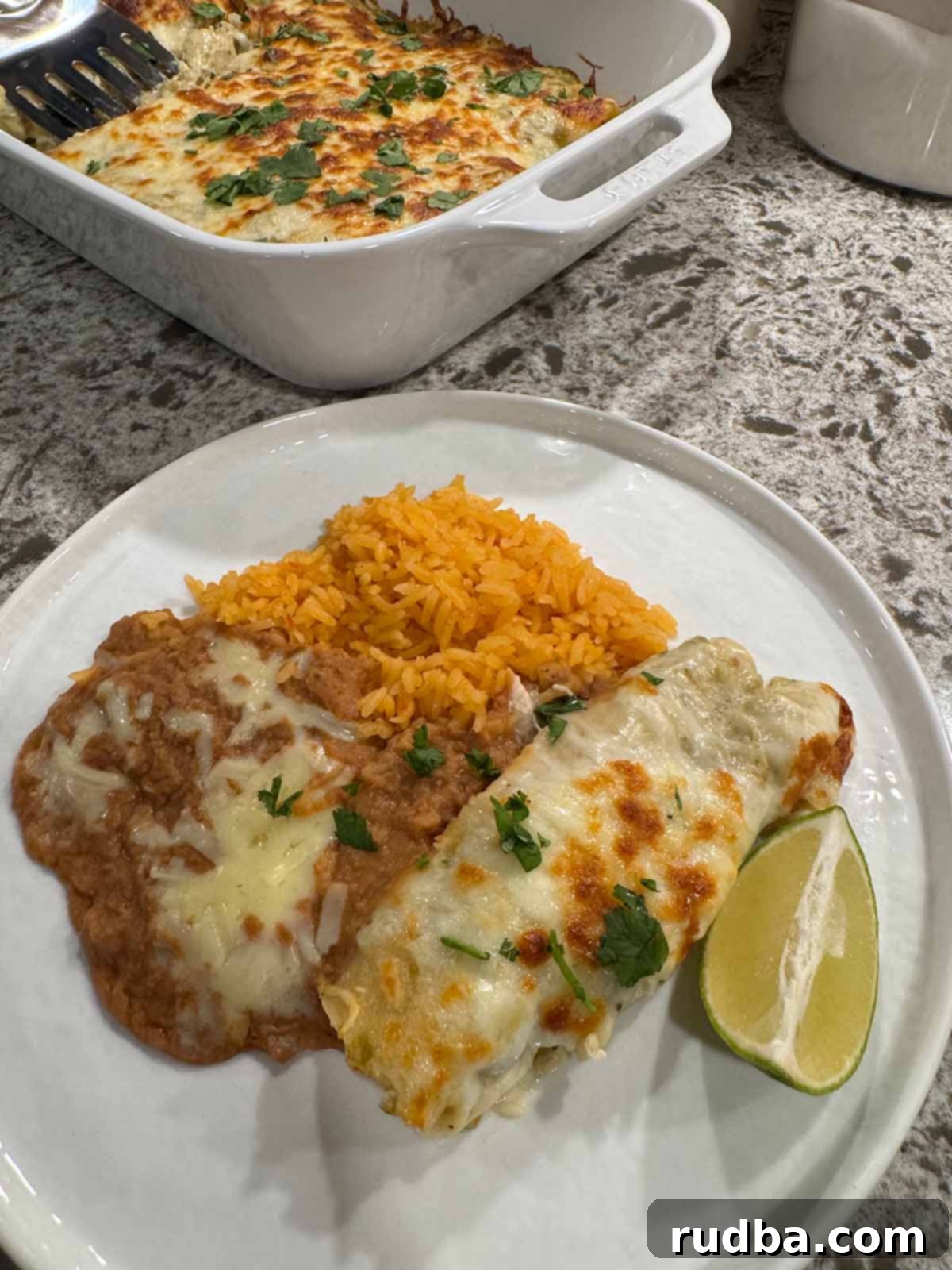Ultimate Green Chile Chicken Enchiladas 2 Delicious Green Chile Chicken Enchiladas with a side of vibrant yellow Mexican rice and creamy refried beans, ready to be enjoyed.
