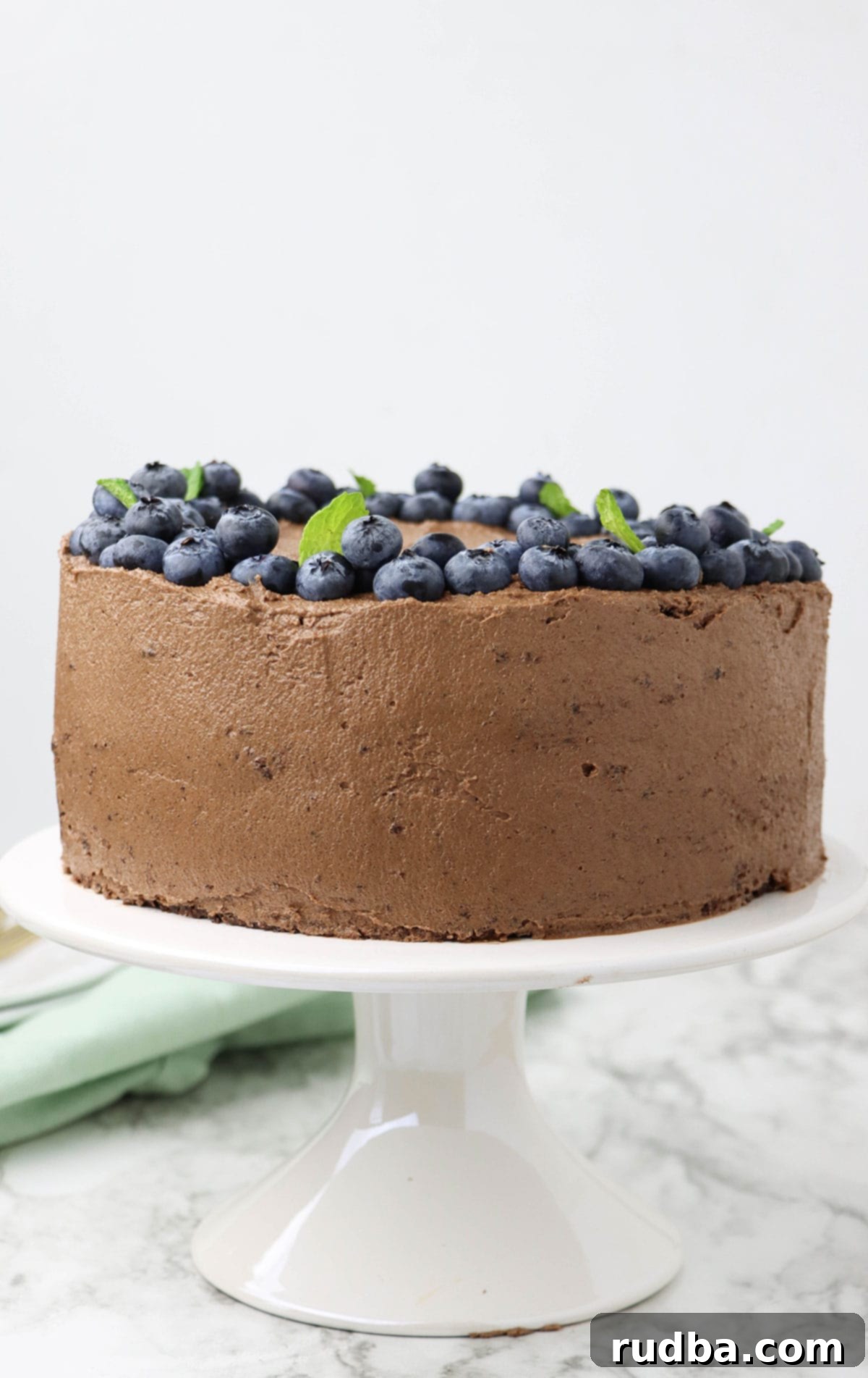 An entire two-layer chocolate cake on a white cake stand, beautifully frosted and ready to be served.