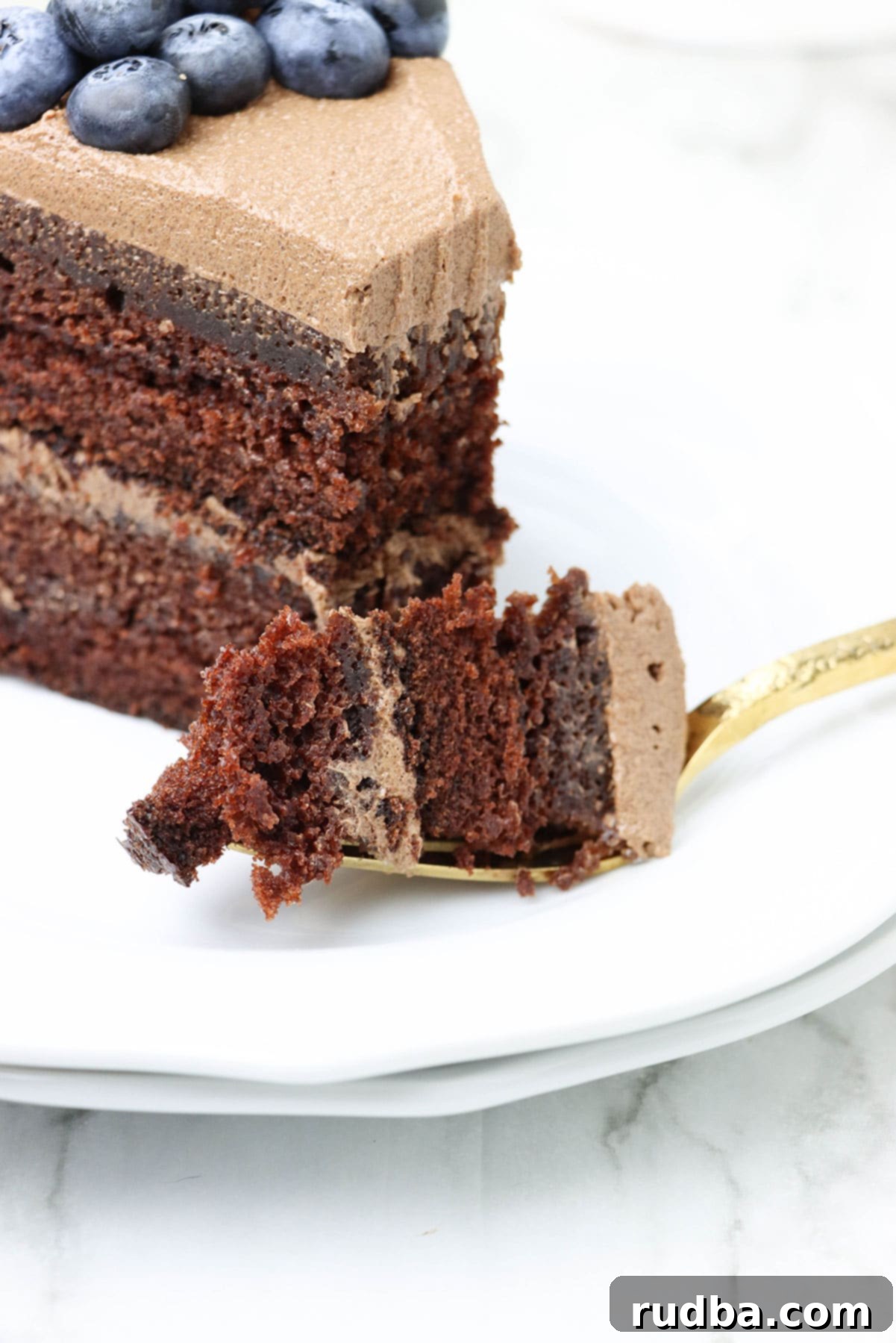 A slice of chocolate cake on a white plate with a gold fork, ready to be enjoyed.
