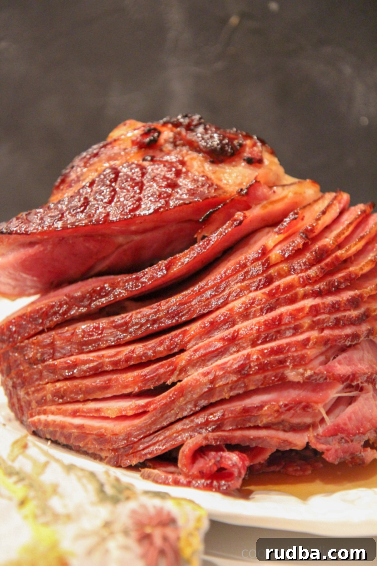 A baked ham with brown sugar glaze on a platter with a dark backdrop. 