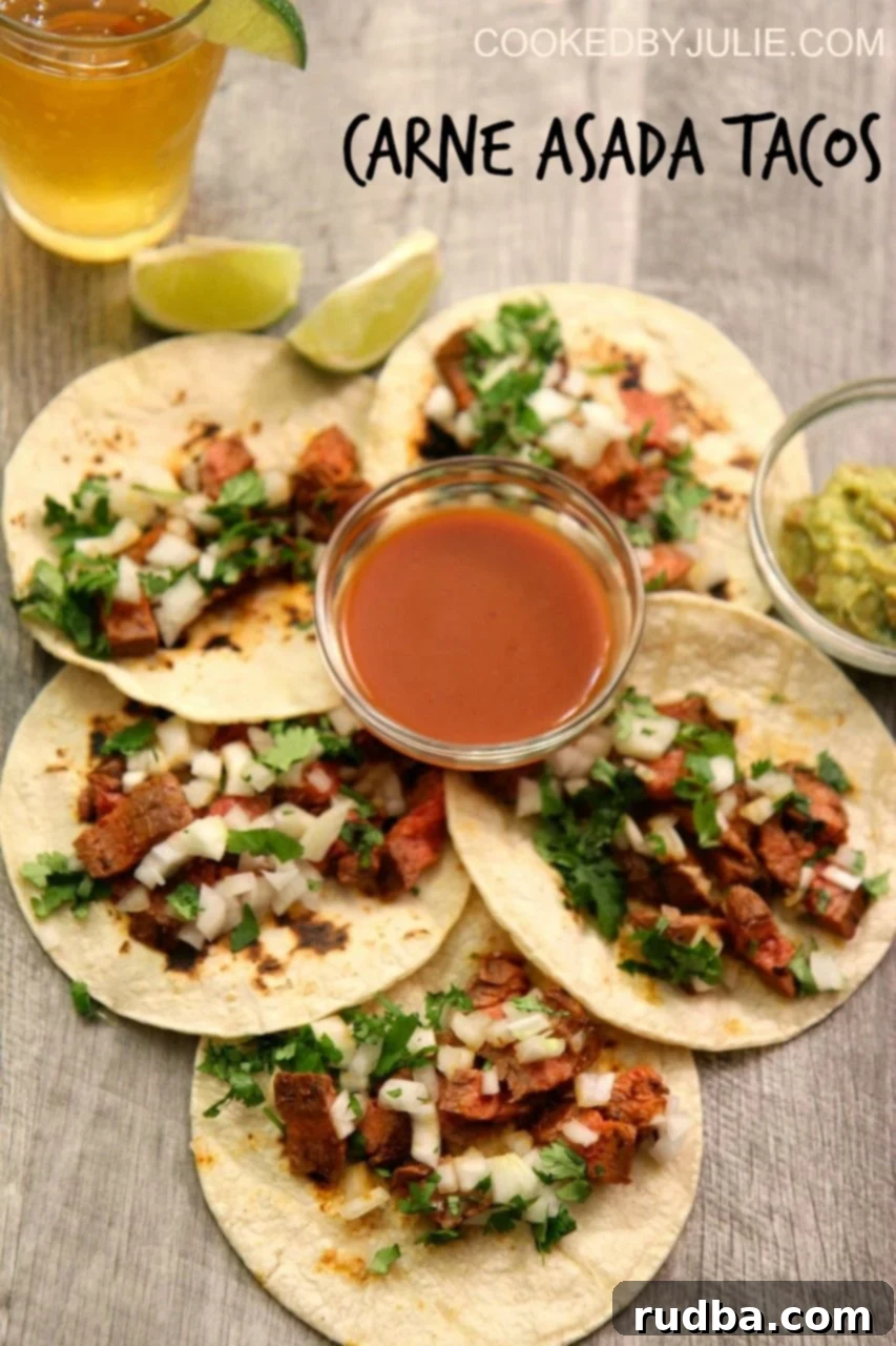 A close-up shot of perfectly assembled homemade Carne Asada Tacos, featuring tender steak, fresh onions, and cilantro, by Cooked by Julie.
