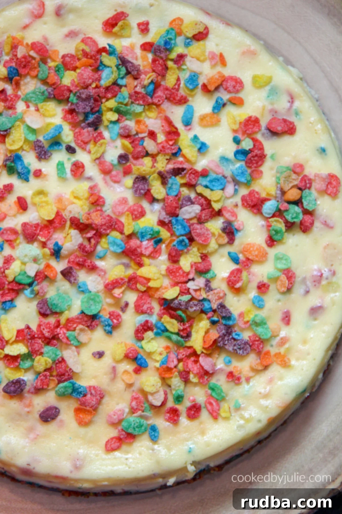 Closeup of a slice of Fruity Pebble Cheesecake, showing the colorful cereal layers in the crust and topping