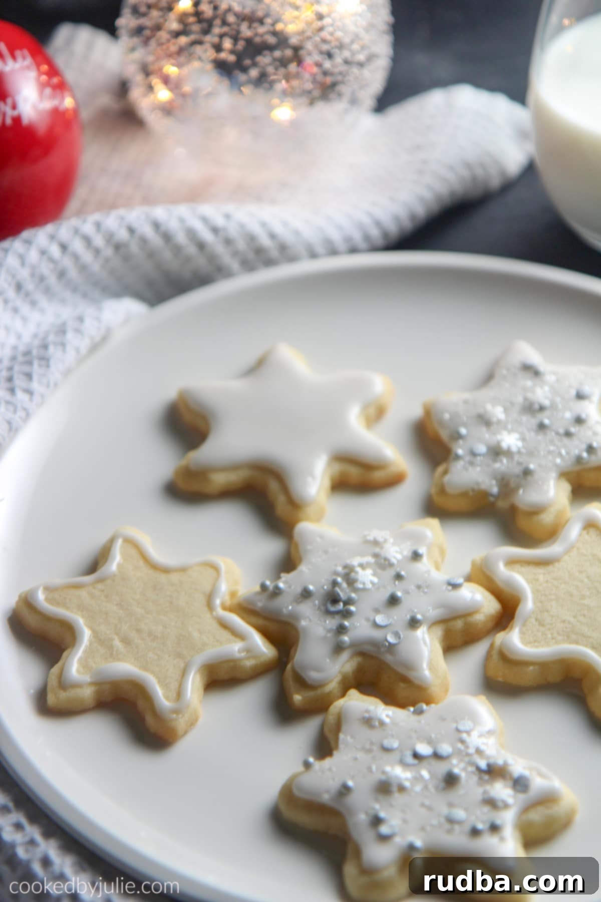 Six sugar cookies with a white towel, a glass of milk, and two festive Christmas tree ornaments, creating a cozy holiday scene.