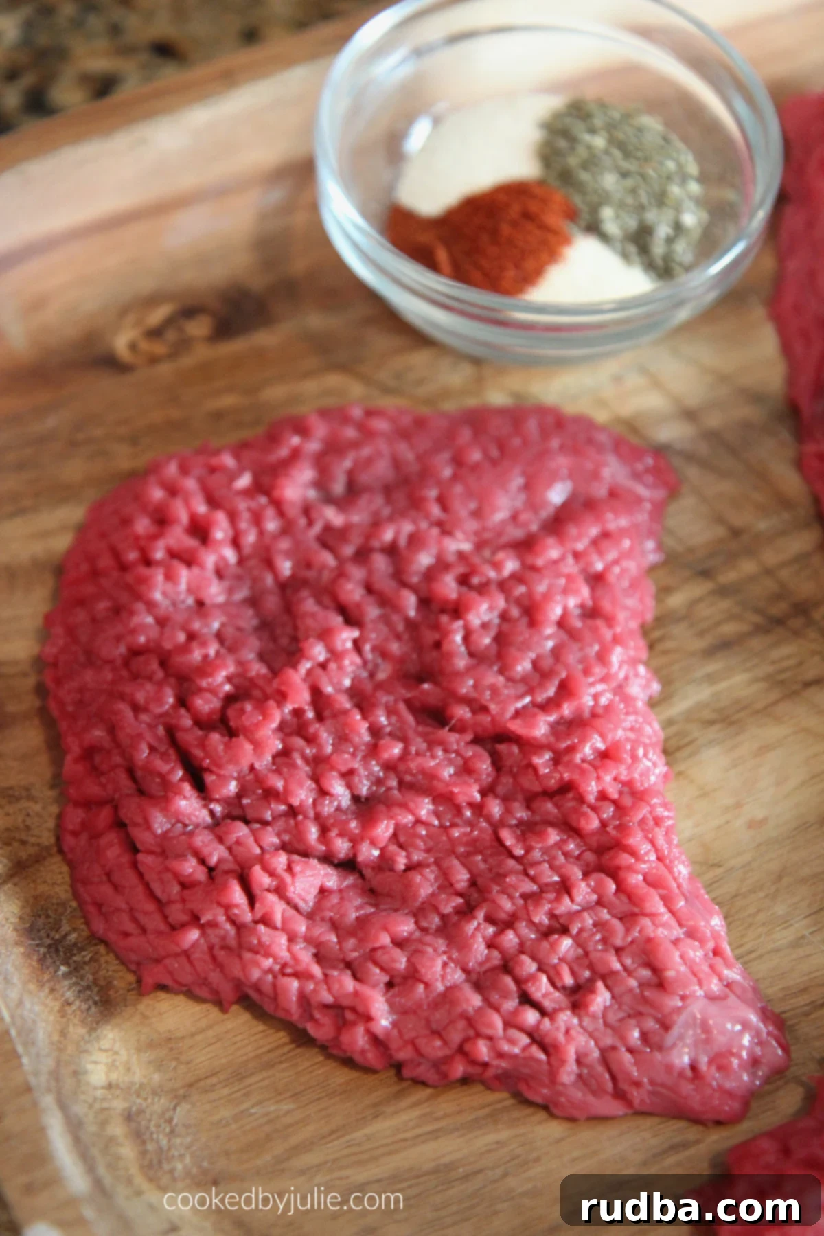 Raw beef steak on a cutting board with a small bowl of spices on the side, ready for seasoning. The vibrant red of the meat contrasts with the earthy tones of the spices, promising a burst of flavor.