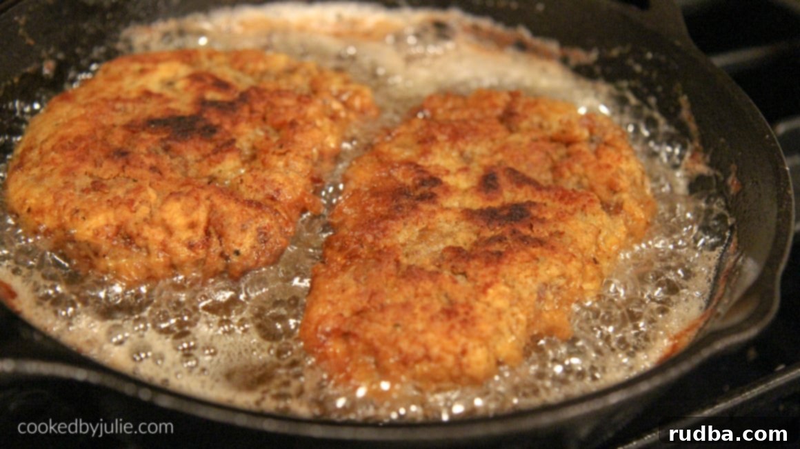 Two perfectly golden-brown chicken fried steak cutlets sizzling and frying in an iron skillet filled with hot oil, showcasing the development of their crispy crust.