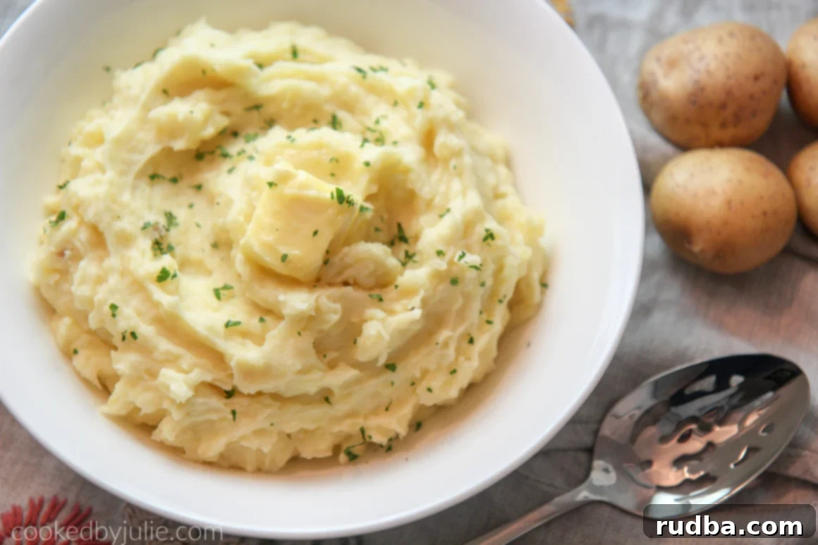 mashed potatoes in a white bowl with a spoon and raw potatoes on the side 