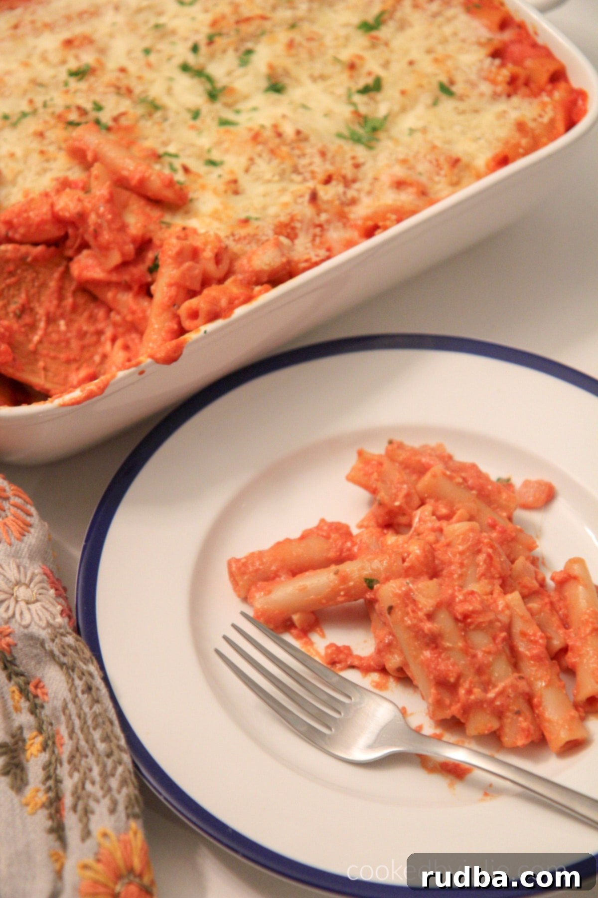 A plate of baked ziti with melted cheese and sauce, garnished with fresh herbs.