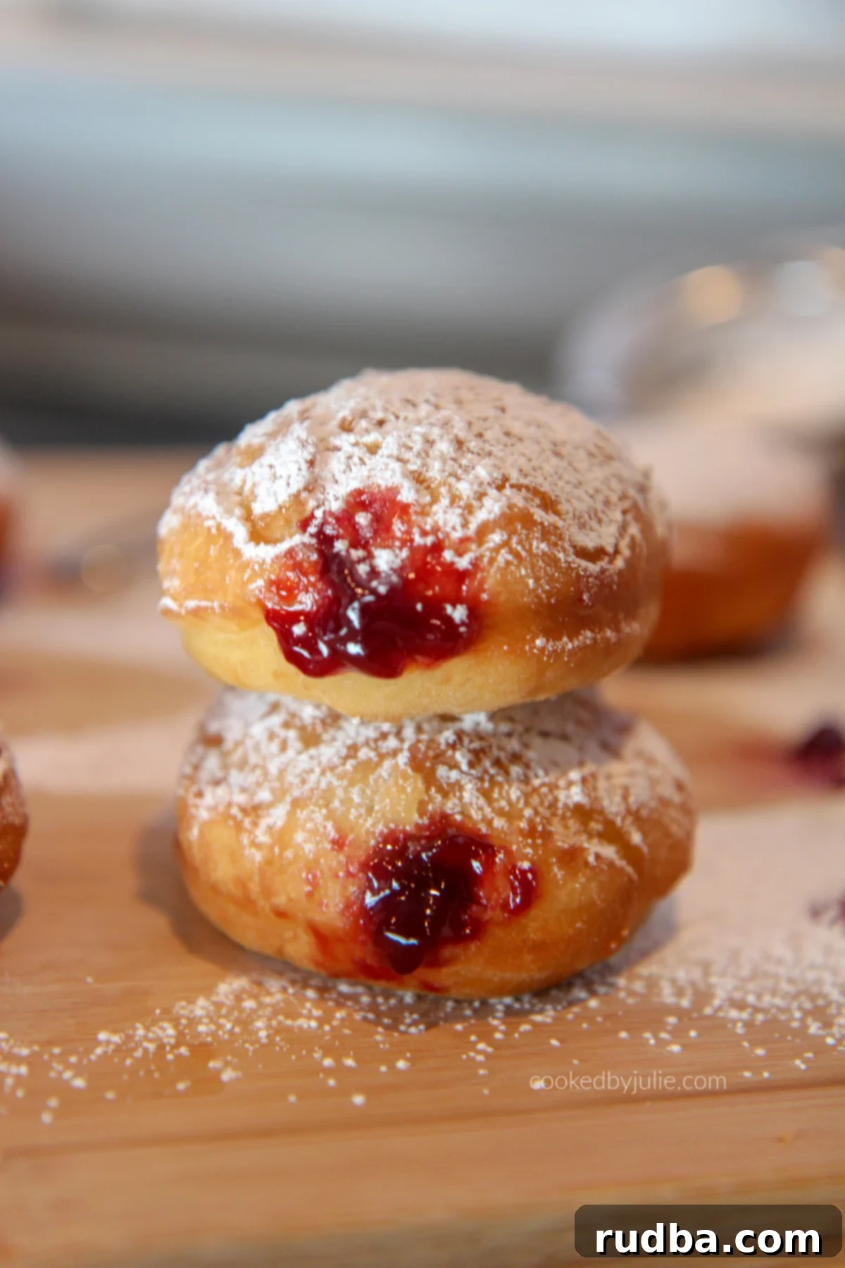 Pillowy homemade jelly donuts with a light dusting of powdered sugar, stacked on a rustic wooden board