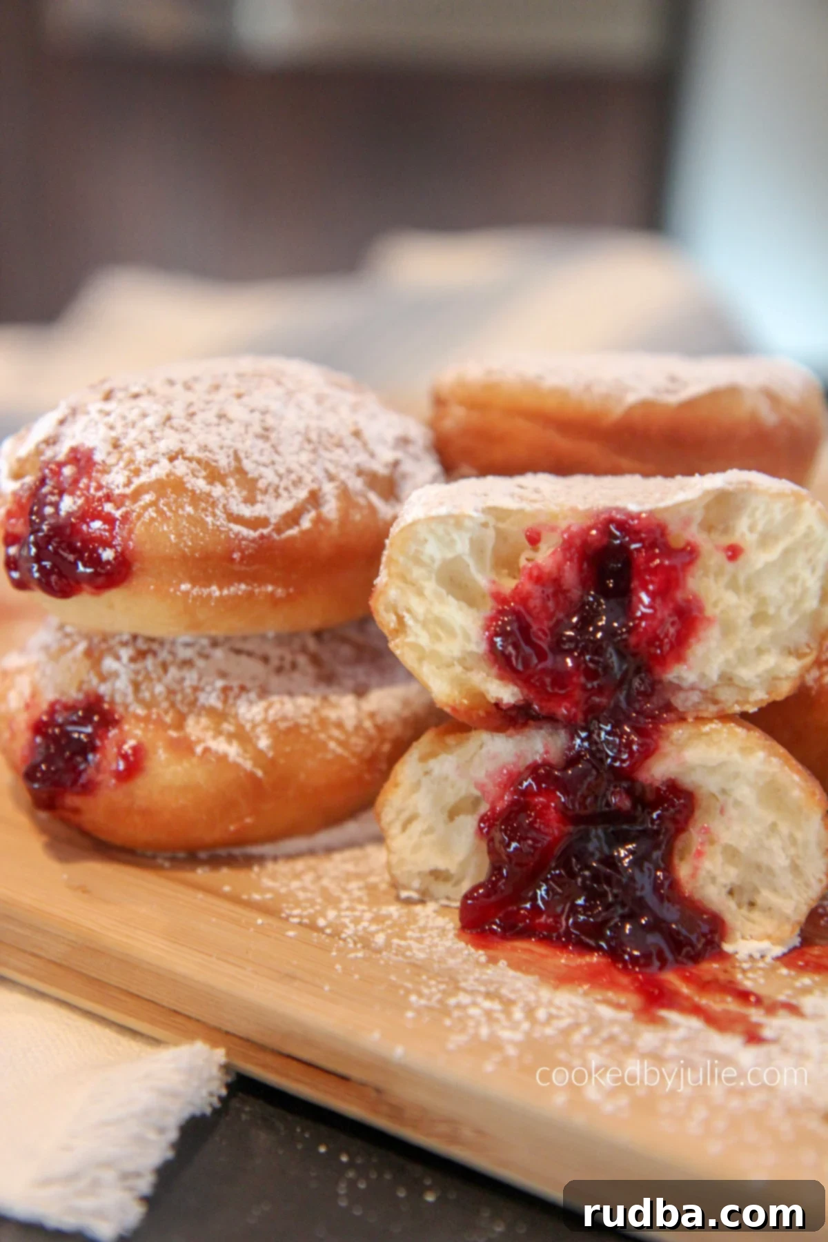 A cross-section of a homemade powdered sugar jelly donut, showing the luscious raspberry jelly filling oozing out