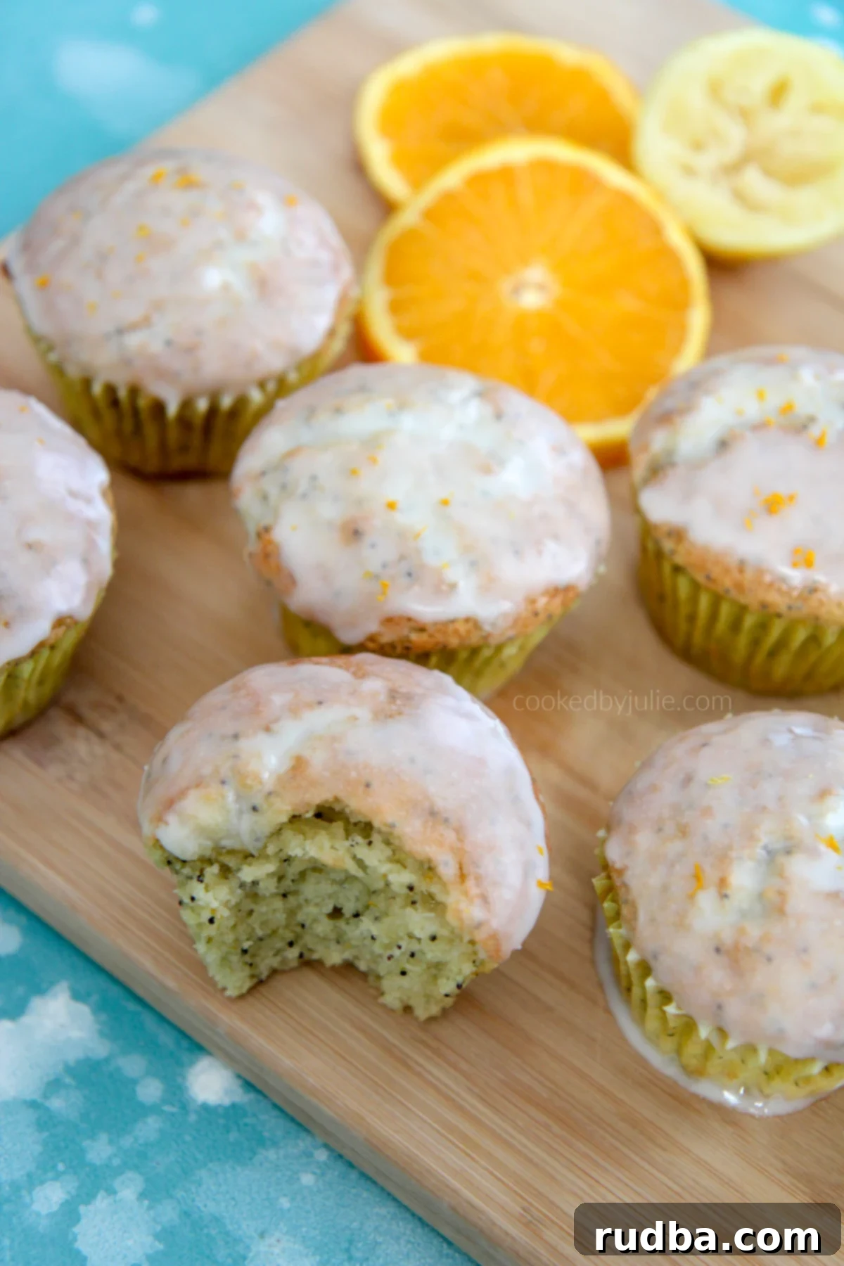 A selection of golden-brown orange lemon poppy seed muffins on a rustic wooden board, garnished with fresh orange slices, highlighting their soft texture and zesty appeal.