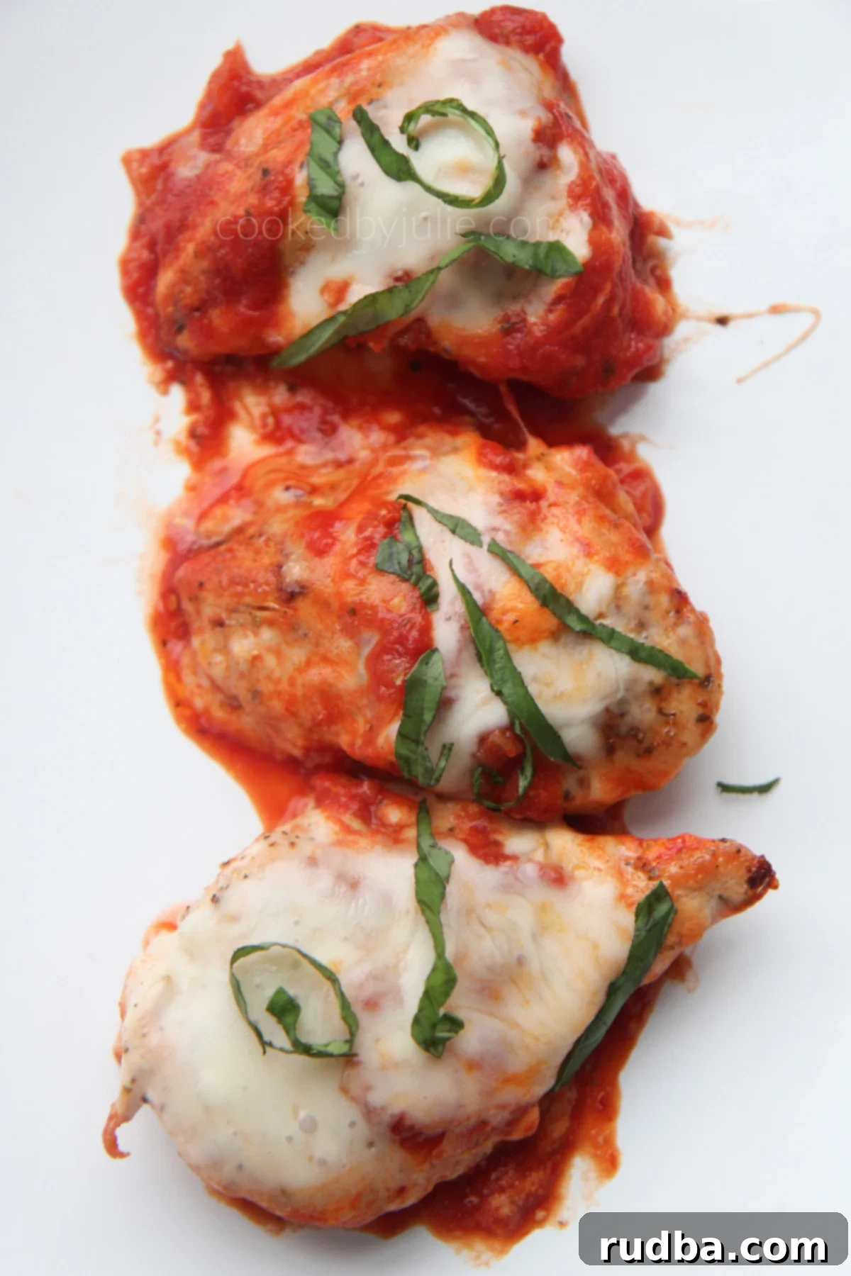 Three servings of grilled chicken parmesan with sauce, melted cheese, and fresh basil, elegantly plated on white dishes.