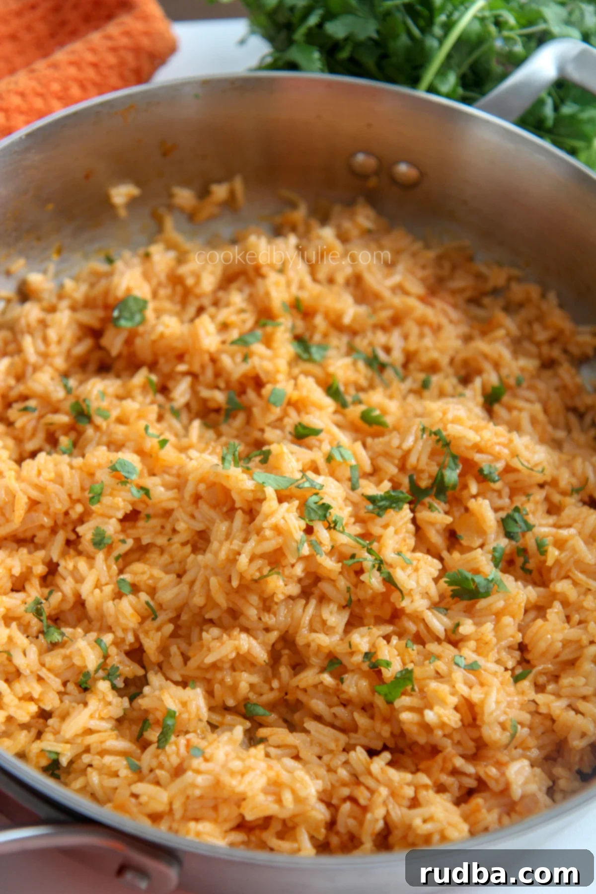 A skillet filled with Spanish rice with an orange kitchen towel and fresh cilantro in the background