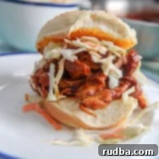 Ultimate BBQ Pulled Chicken Stack 5 bbq pulled chicken sandwich on top of a white plate with pieces of coleslaw on the plate